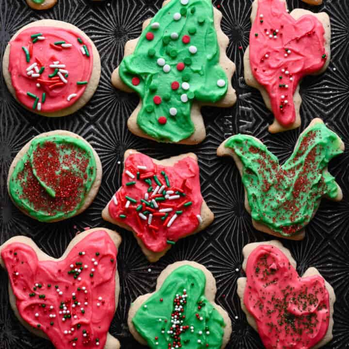 Frosted Sour Cream Cookies in a variety of shapes on a textured baking pan.