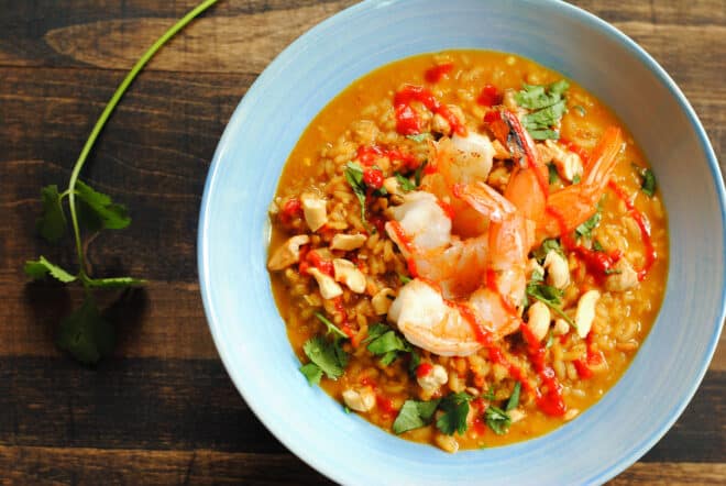 Shallow light blue bowl of spicy rice dish with shrimp, on wooden background.