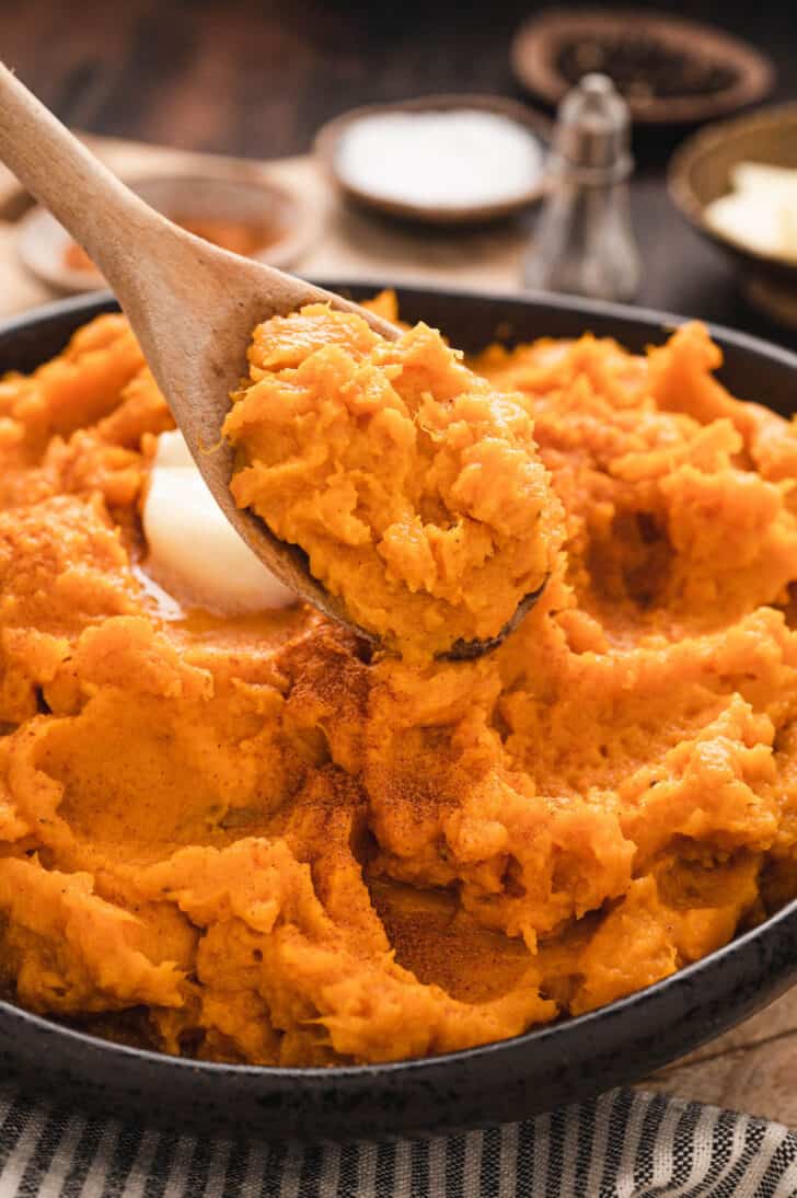 Instant Pot Mashed Sweet Potatoes in a black bowl with a wooden spoon serving some.