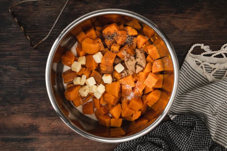 Cubed orange vegetables, butter, brown sugar and spices in a metal bowl.