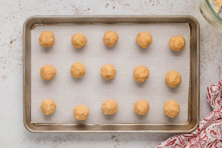 15 small balls of light brown dough on a rimmed baking pan.
