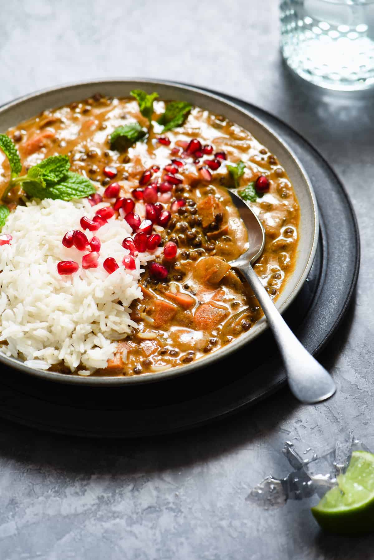 Closeup of a spoon digging into a lentil stew in a shallow gray bowl.