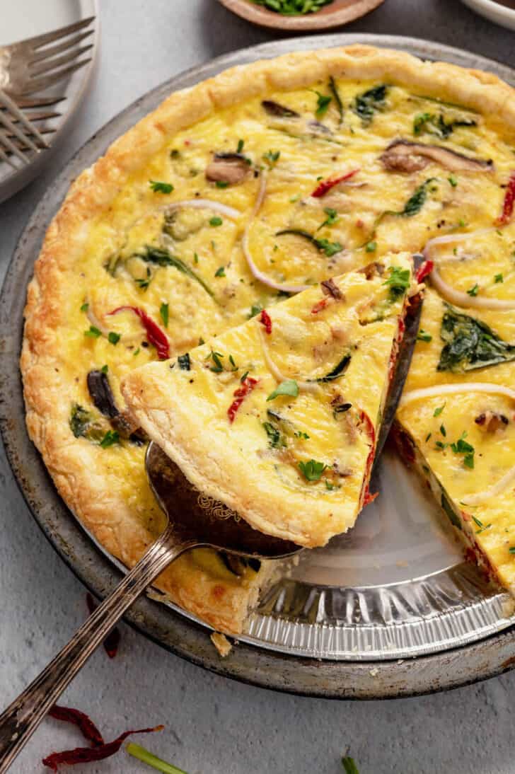A slice of vegetarian quiche being lifted out of a full quiche in a metal pie plate.